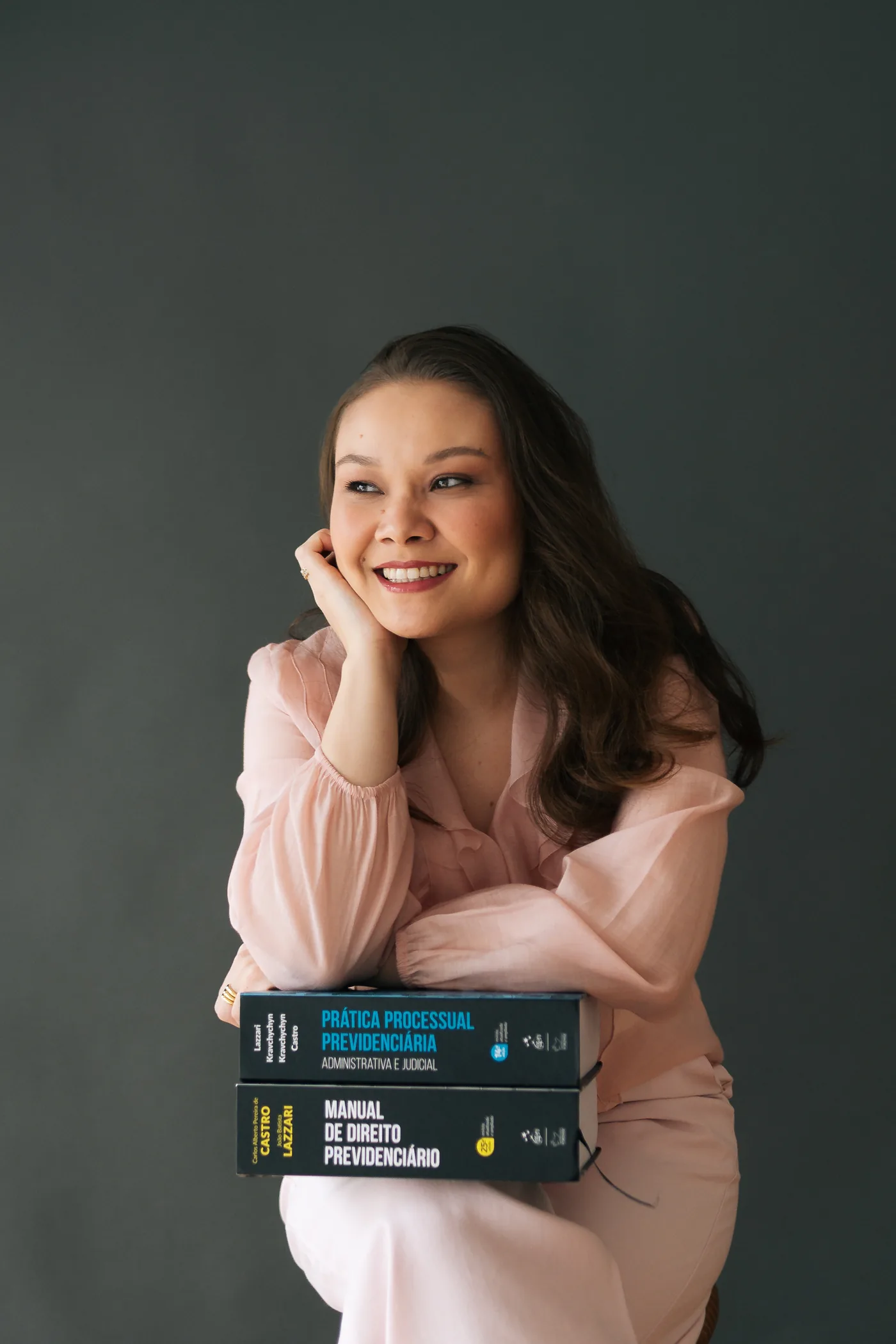 Ana Beatriz Hayasaki sorrindo ao lado de livros de Direito Previdenciário